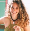 Bea Bazani sorri olhando para a câmera. Uma foto de perfil descontraída e muito iluminada.
